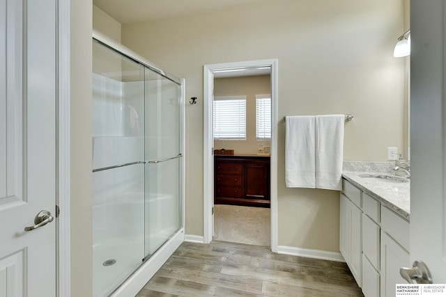 bathroom featuring baseboards, wood finished floors, vanity, and a stall shower