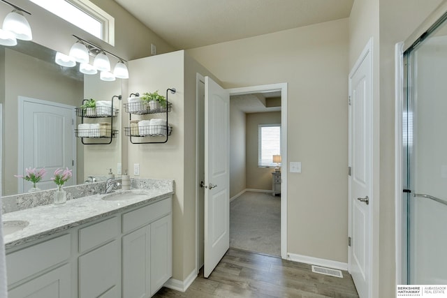 full bath featuring a sink, double vanity, baseboards, visible vents, and wood finished floors