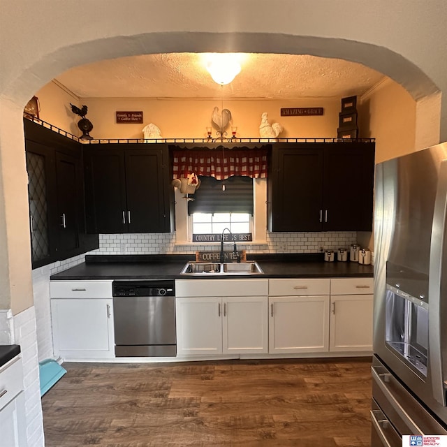 kitchen with arched walkways, a sink, dark wood-style flooring, dark countertops, and appliances with stainless steel finishes