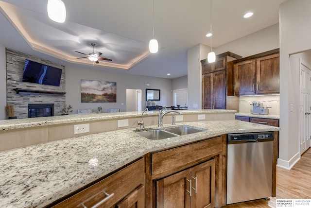 kitchen featuring a stone fireplace, a sink, dishwasher, ceiling fan, and light stone countertops