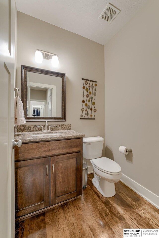 half bathroom featuring wood finished floors, visible vents, toilet, and baseboards