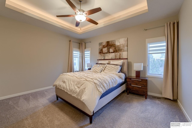 carpeted bedroom featuring ceiling fan, baseboards, a tray ceiling, and visible vents