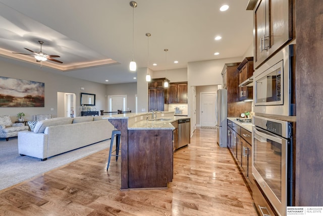 kitchen with light wood finished floors, stainless steel appliances, a sink, open floor plan, and a kitchen bar