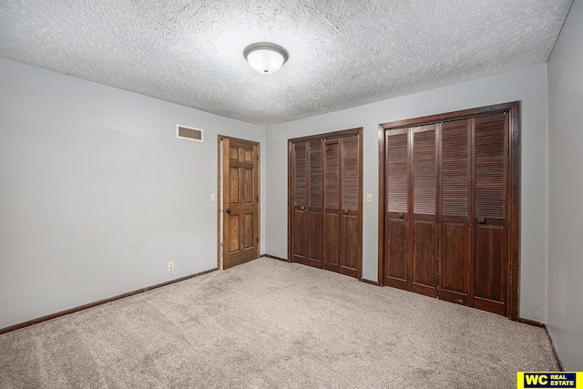 unfurnished bedroom with a textured ceiling, visible vents, baseboards, carpet, and multiple closets
