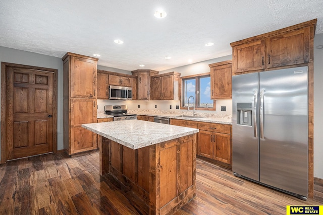 kitchen with a sink, appliances with stainless steel finishes, a kitchen island, light countertops, and dark wood finished floors