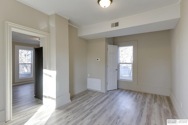 spare room featuring visible vents, light wood-style floors, ornamental molding, and a healthy amount of sunlight