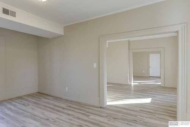 empty room with light wood finished floors, baseboards, visible vents, and ornamental molding