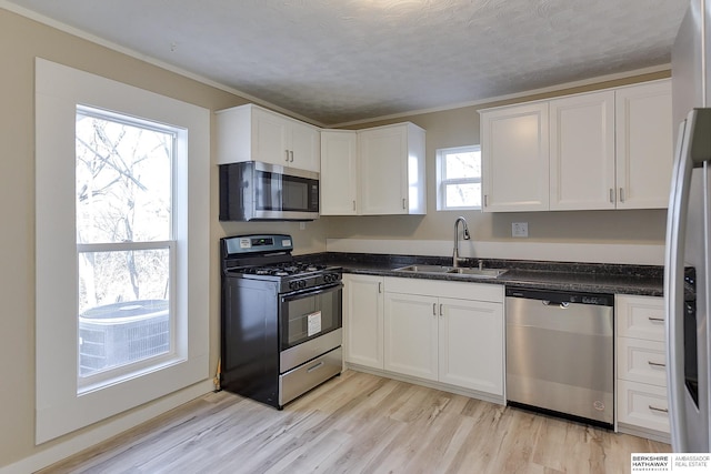 kitchen featuring a sink, light wood-type flooring, crown molding, appliances with stainless steel finishes, and white cabinetry
