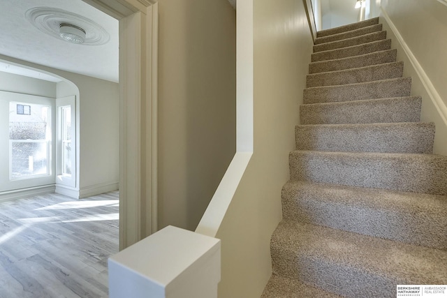 stairs featuring baseboards, wood finished floors, and arched walkways