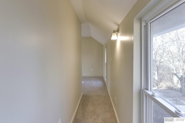 hallway with lofted ceiling, baseboards, and light carpet