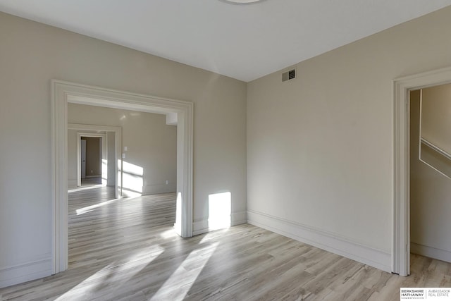 empty room featuring light wood-type flooring, visible vents, and baseboards