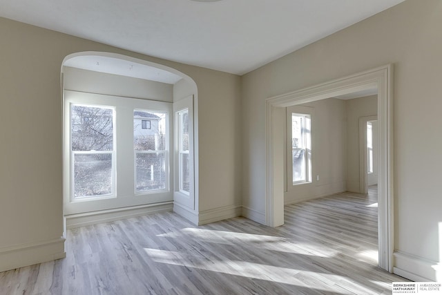 spare room with arched walkways, wood finished floors, and baseboards