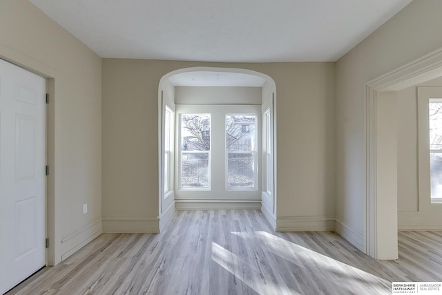 unfurnished room with baseboards, wood finished floors, and arched walkways