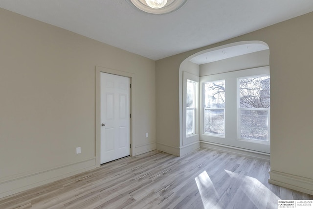 empty room featuring arched walkways, light wood finished floors, and baseboards