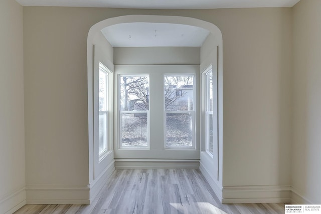 spare room featuring arched walkways, wood finished floors, and baseboards