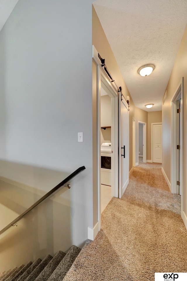 hallway featuring a barn door, baseboards, and carpet