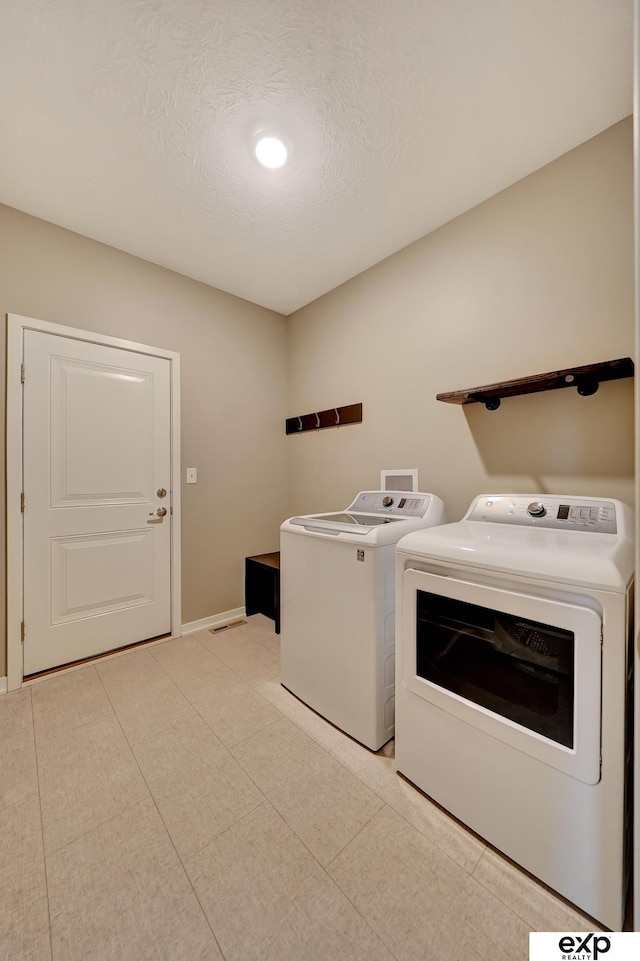 clothes washing area with baseboards, a textured ceiling, separate washer and dryer, and laundry area