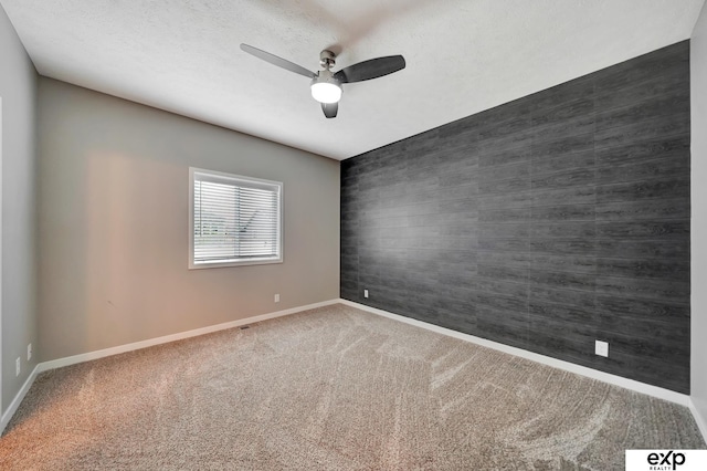 carpeted empty room with baseboards, an accent wall, and ceiling fan