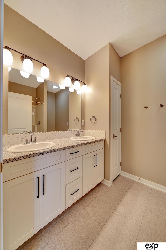 bathroom with a shower, baseboards, a sink, and double vanity