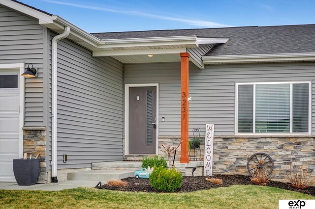 doorway to property featuring an attached garage, roof with shingles, and stone siding