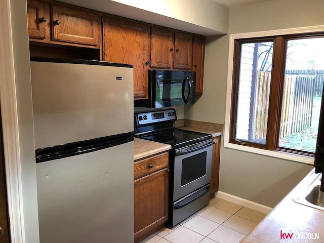 kitchen with brown cabinets, appliances with stainless steel finishes, and light tile patterned flooring