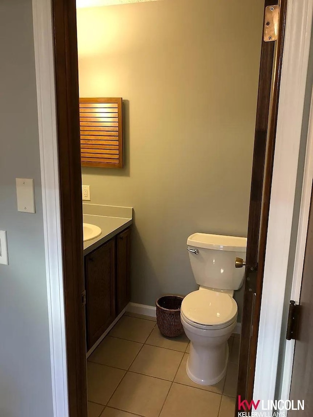 half bathroom with baseboards, tile patterned flooring, vanity, and toilet