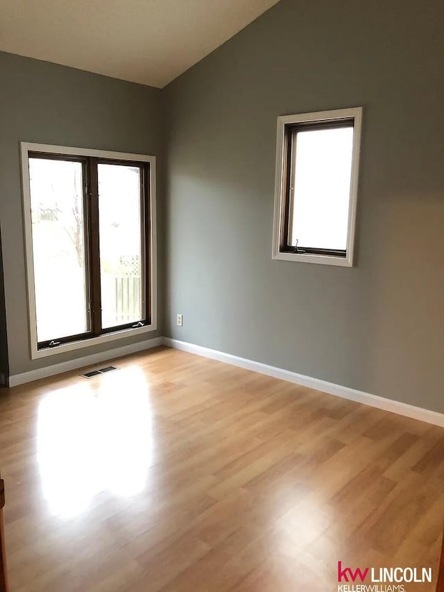 empty room featuring vaulted ceiling, baseboards, light wood-style floors, and visible vents