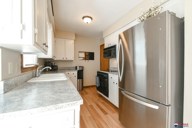 kitchen with a sink, black appliances, light wood finished floors, light countertops, and white cabinetry