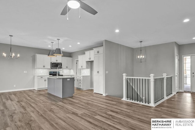 kitchen featuring light wood-style flooring, stainless steel microwave, white cabinetry, and a center island with sink