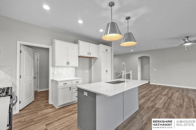 kitchen featuring stainless steel gas range oven, a sink, arched walkways, light wood-style floors, and white cabinetry