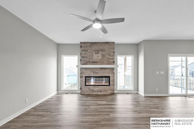 unfurnished living room featuring baseboards, wood finished floors, a ceiling fan, and a large fireplace