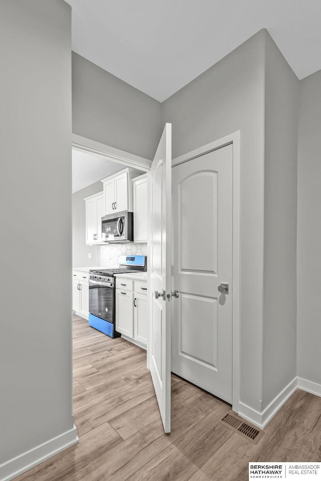 kitchen with tasteful backsplash, light wood-type flooring, stainless steel appliances, white cabinets, and visible vents