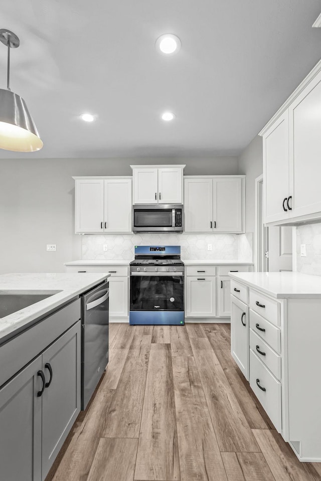 kitchen with decorative backsplash, light wood-type flooring, light countertops, white cabinets, and appliances with stainless steel finishes