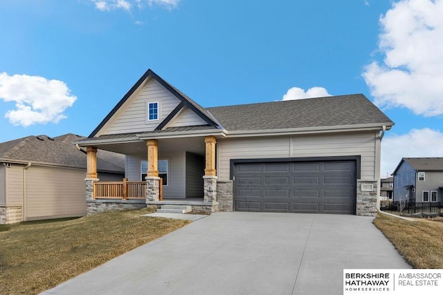 craftsman-style house featuring driveway, stone siding, covered porch, an attached garage, and a front yard