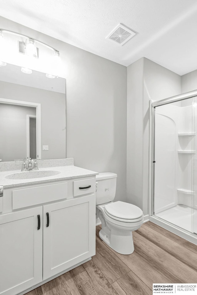 full bathroom with a shower stall, toilet, wood finished floors, and visible vents