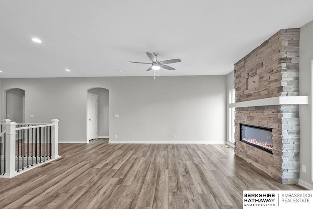 unfurnished living room featuring arched walkways, recessed lighting, a ceiling fan, wood finished floors, and a fireplace