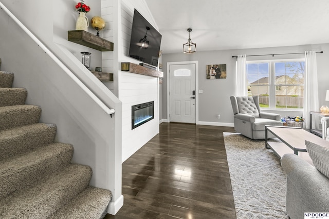 living area with dark wood-type flooring, a large fireplace, stairway, and baseboards