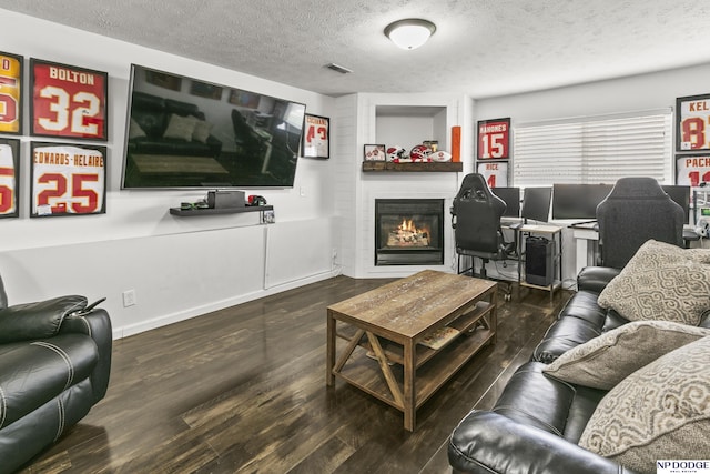 living room with wood finished floors, a textured ceiling, a fireplace, baseboards, and visible vents
