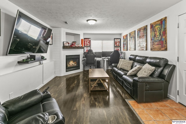 living area with a textured ceiling, wood finished floors, visible vents, and a fireplace