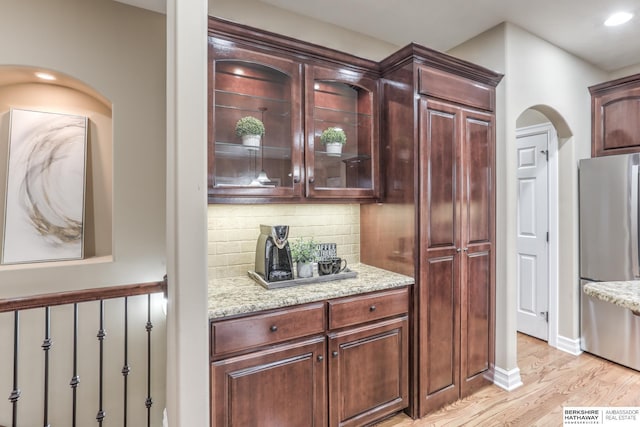 bar with freestanding refrigerator, recessed lighting, arched walkways, light wood-style flooring, and backsplash