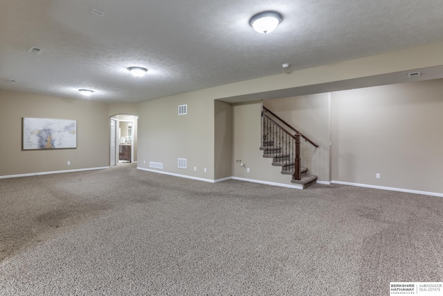 finished below grade area featuring arched walkways, a textured ceiling, stairs, and carpet