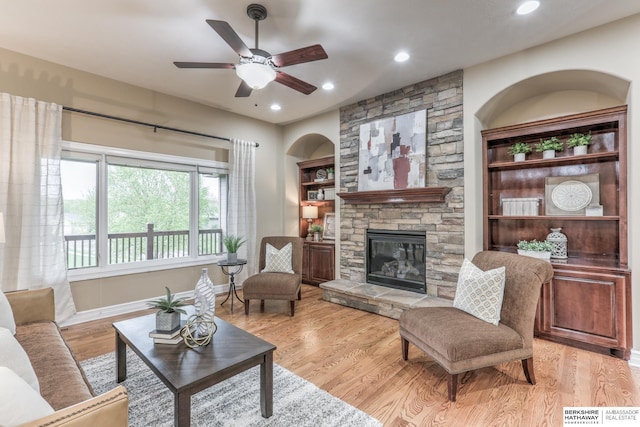 living area with a ceiling fan, recessed lighting, a stone fireplace, and light wood finished floors