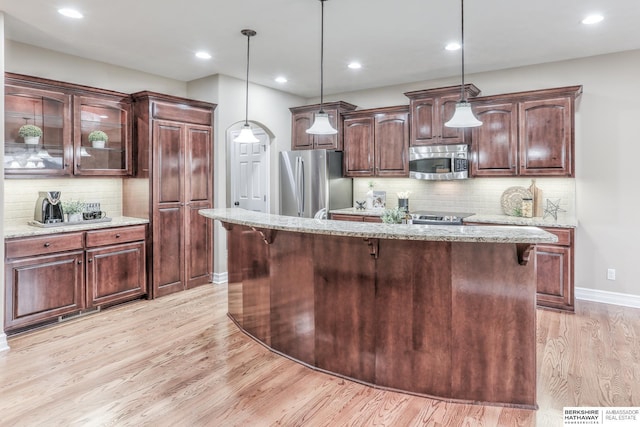 kitchen featuring light stone countertops, baseboards, light wood finished floors, backsplash, and stainless steel appliances