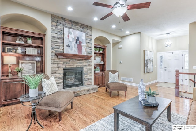 living area with a fireplace, built in features, light wood-style flooring, baseboards, and visible vents