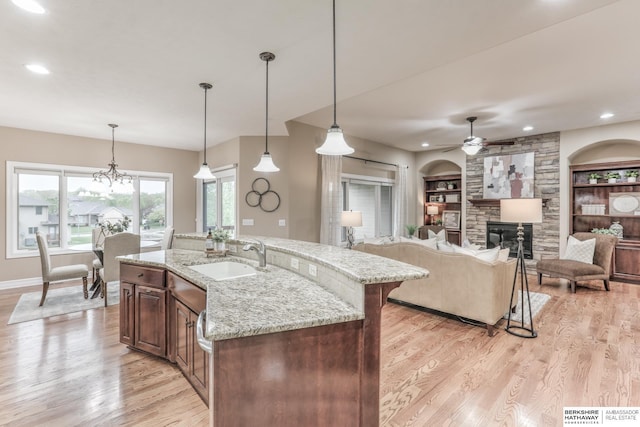 kitchen with a ceiling fan, a fireplace, light stone countertops, light wood-type flooring, and a sink