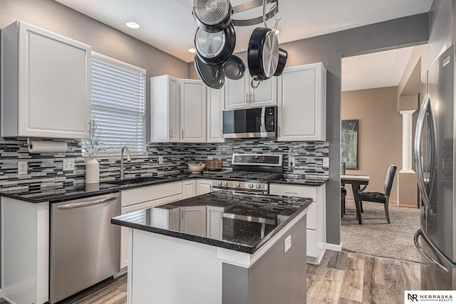 kitchen featuring white cabinets, a sink, stainless steel appliances, decorative backsplash, and light wood-type flooring