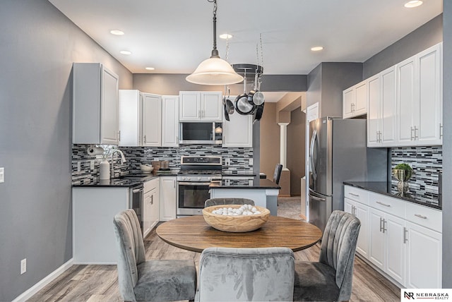 kitchen featuring dark countertops, tasteful backsplash, a sink, stainless steel appliances, and light wood-type flooring
