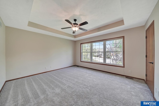 spare room featuring light colored carpet, ceiling fan, a tray ceiling, and baseboards