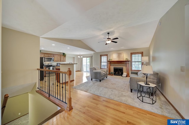 living area featuring baseboards, light wood finished floors, vaulted ceiling, a tiled fireplace, and a ceiling fan