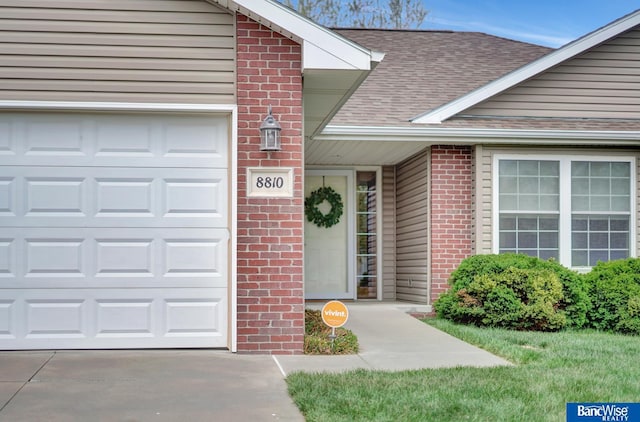entrance to property featuring brick siding, a shingled roof, driveway, and an attached garage